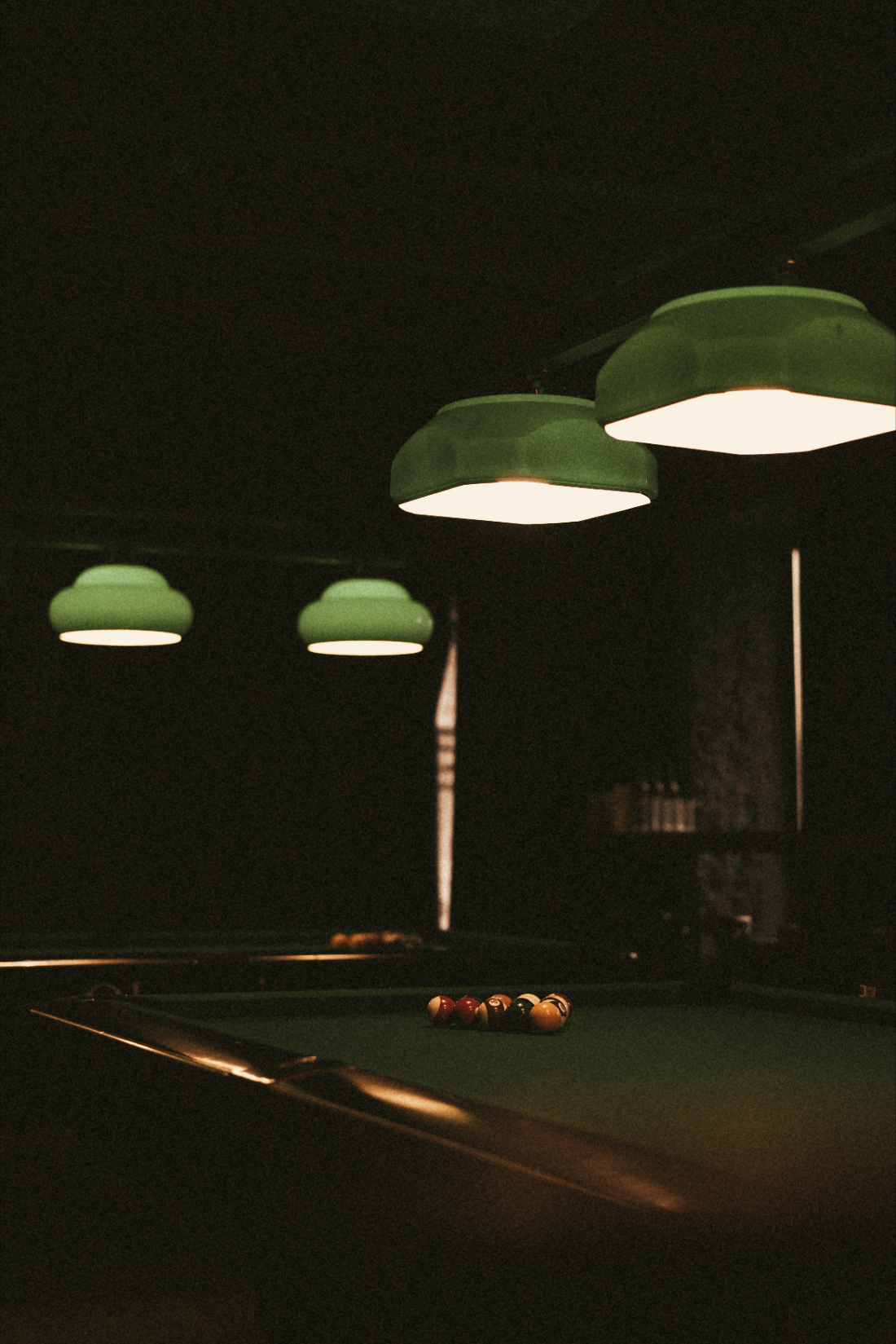 A pool table racked and waiting under low green lamps